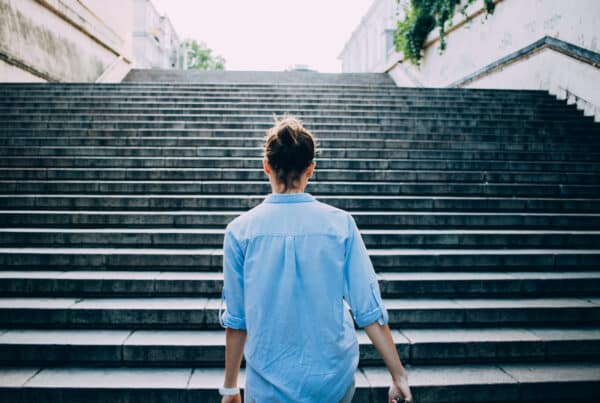 Woman in blue shirt walking up the stairs-- building her momentum and engagement in coaching